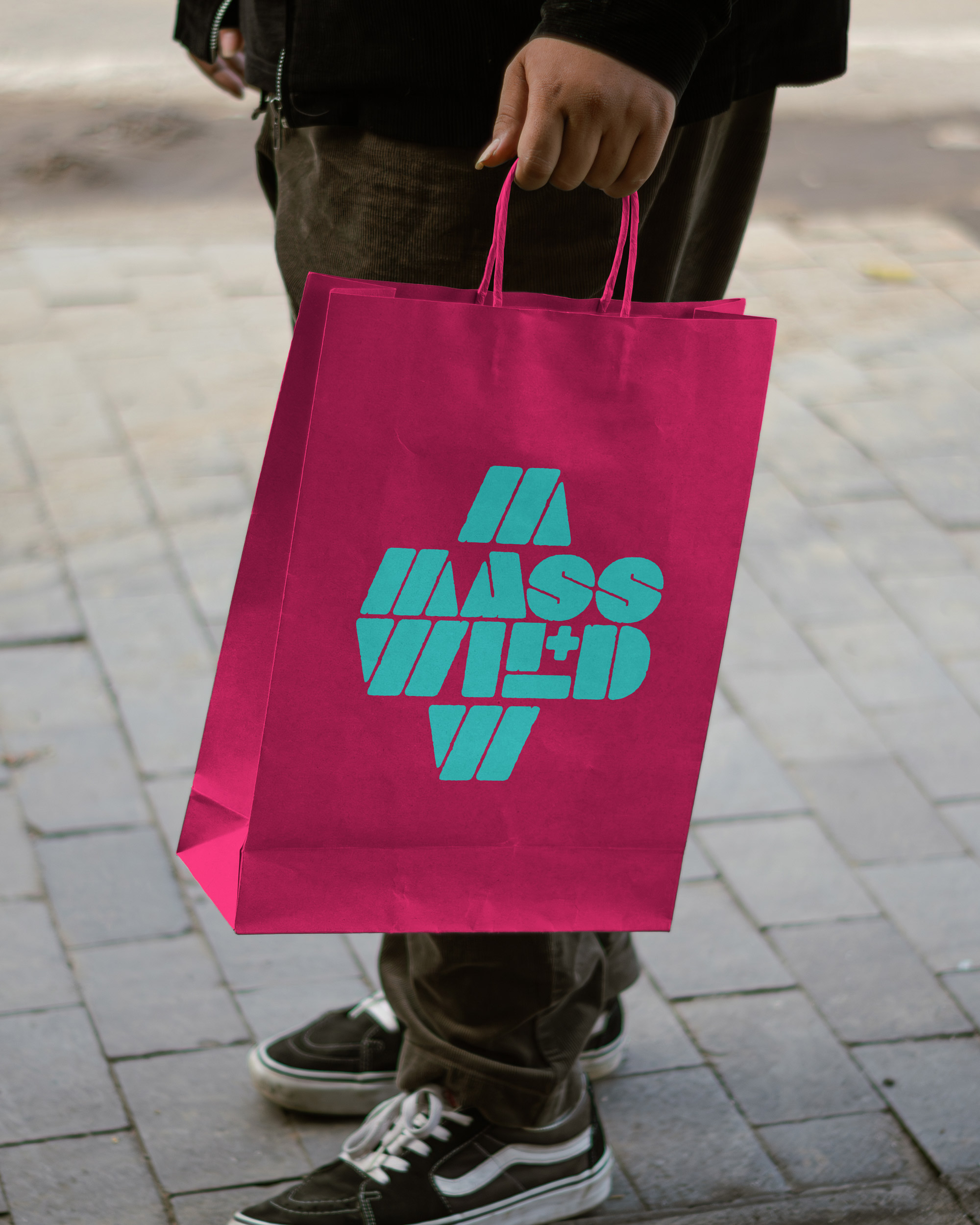 Individual carrying a pink paper bag with "Mass Wild" printed in bold letters, showcasing a stylish shopping design.