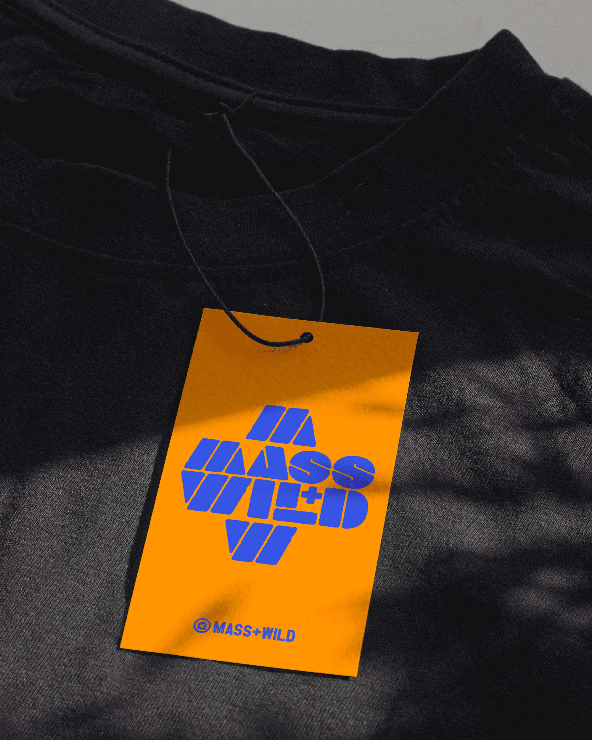 Close-up of a black t-shirt displaying a vibrant blue and orange tag with "Mass+Wild" branding.